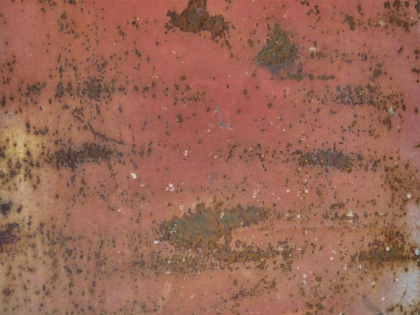 Rust spots texture, spread irregularly and among larger patches on a surface of red painted metal.